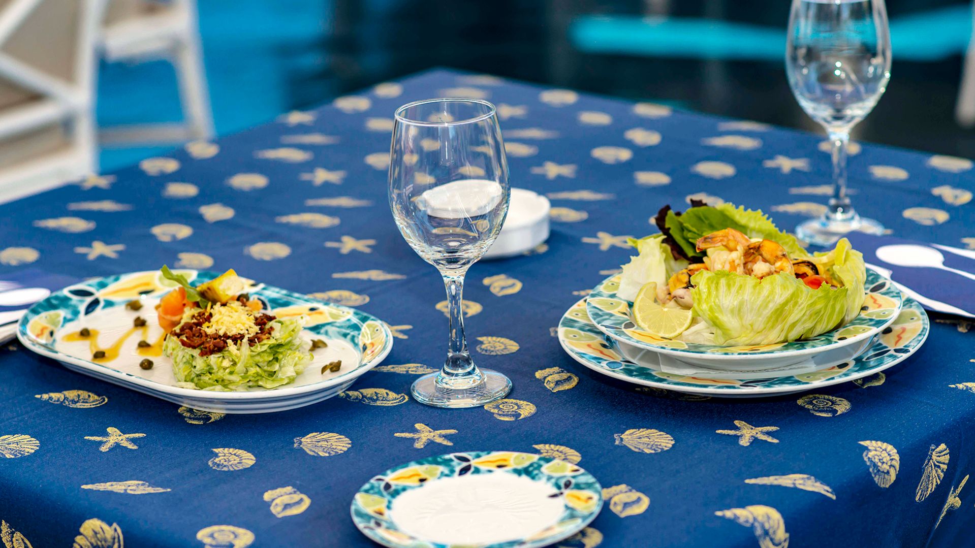 A Blue And White Plate Sitting On Top Of A Table With Wine Glasses